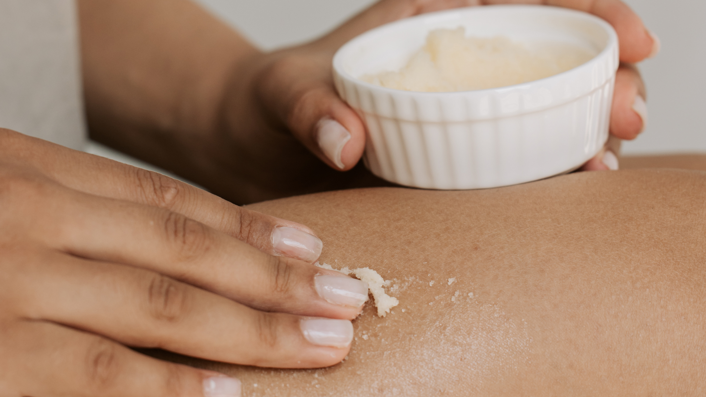 Photo of a container and a hand applying a cream on a skin