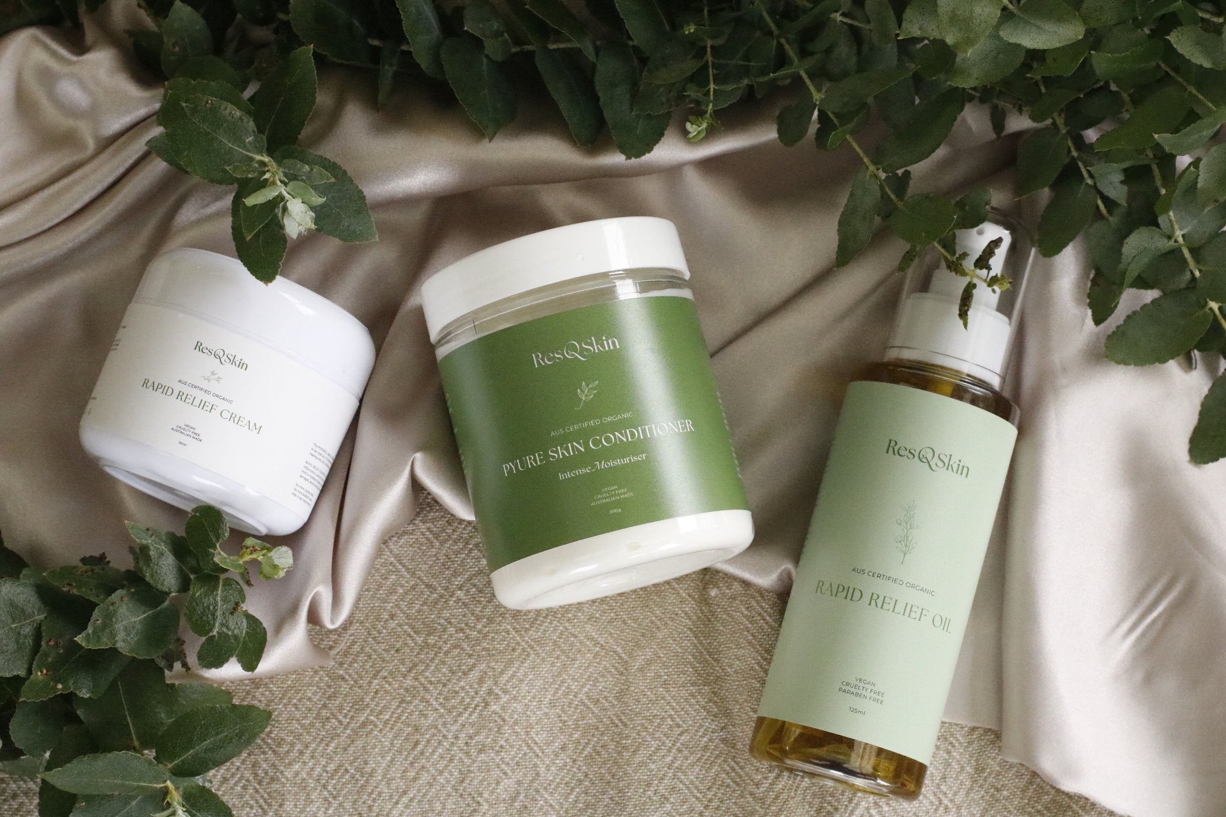 Image of ResQSkin Products, 2 Rapid Relief Cream and a Pyure Skin Conditioner resting on a fabric with leaves hanging out as foreground